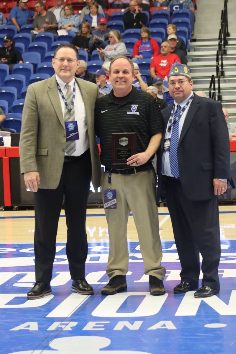 three men standing in a gym and one being presented an award