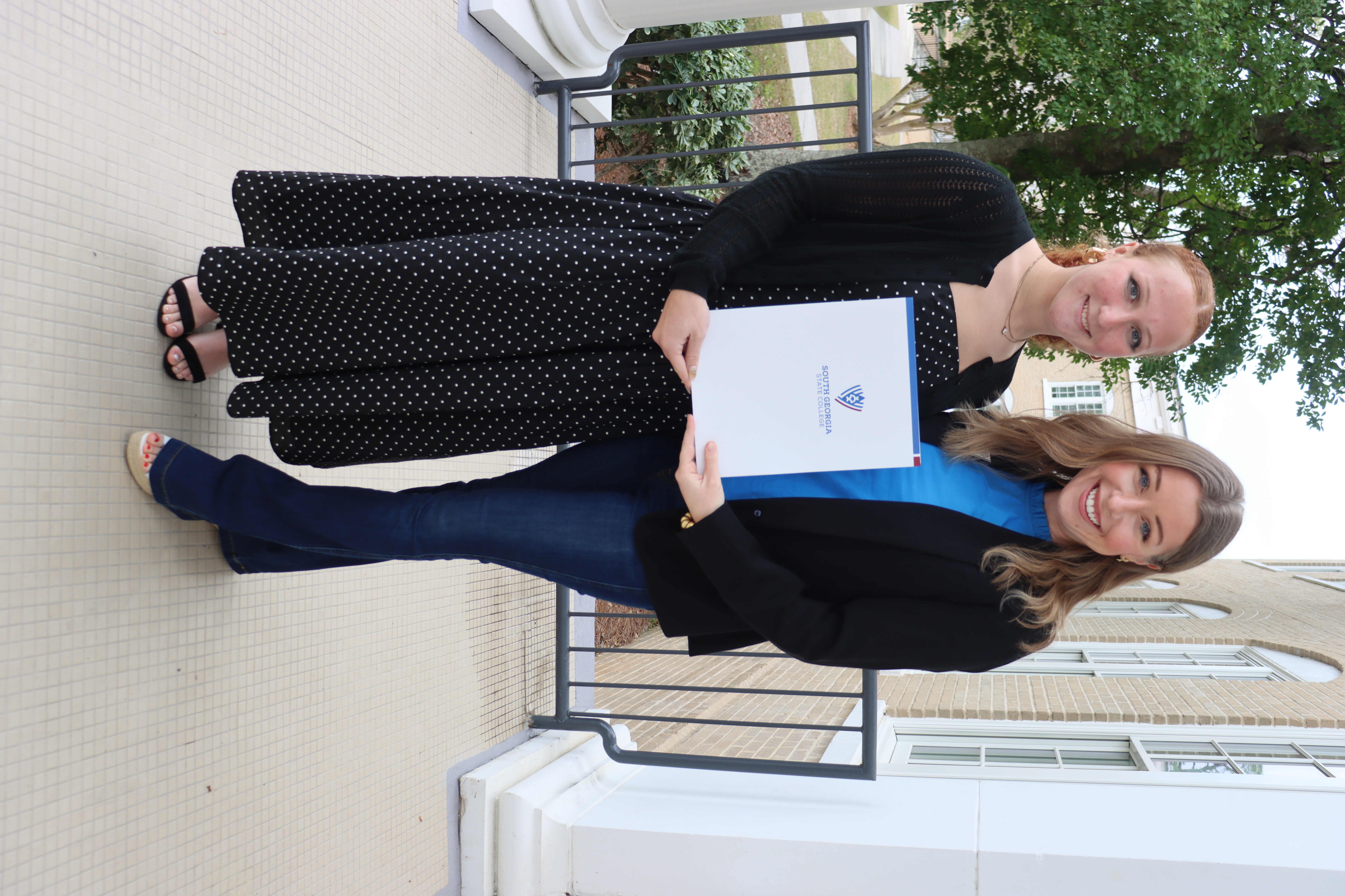 2 females on the front steps holding a certificate